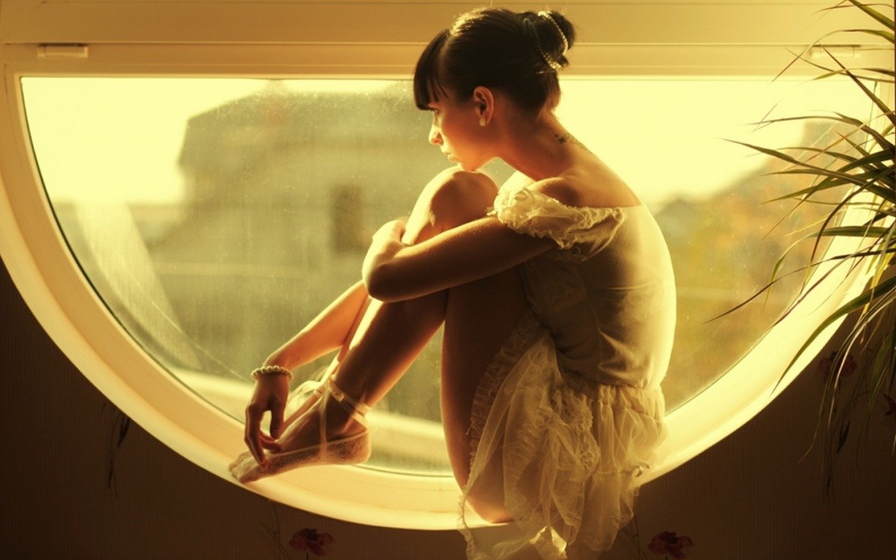 Девушка в платье сидит на окне